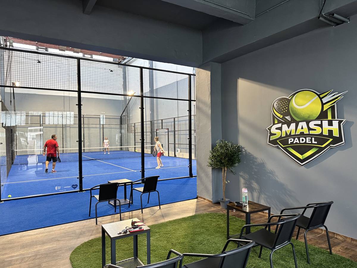 A klub pihenőrésze műfűvel és a falon a Smash Padel logóval, mögötte a pálya